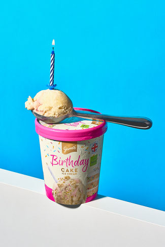 conceptual food photography of  giannis birthday cake flavoured ice cream, with a spoon of ice cream and a candle stuck into the ice cream, set on a bold blue backdrop, harrogate 