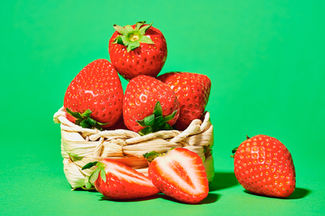 red strawberries placed in a wooden bucket set on a bold green backdrop, food photography, North Yorkshire 