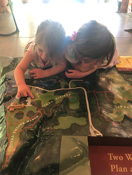 Two girls hover over a two dimensional map of Schlitz Audubon Nature Center