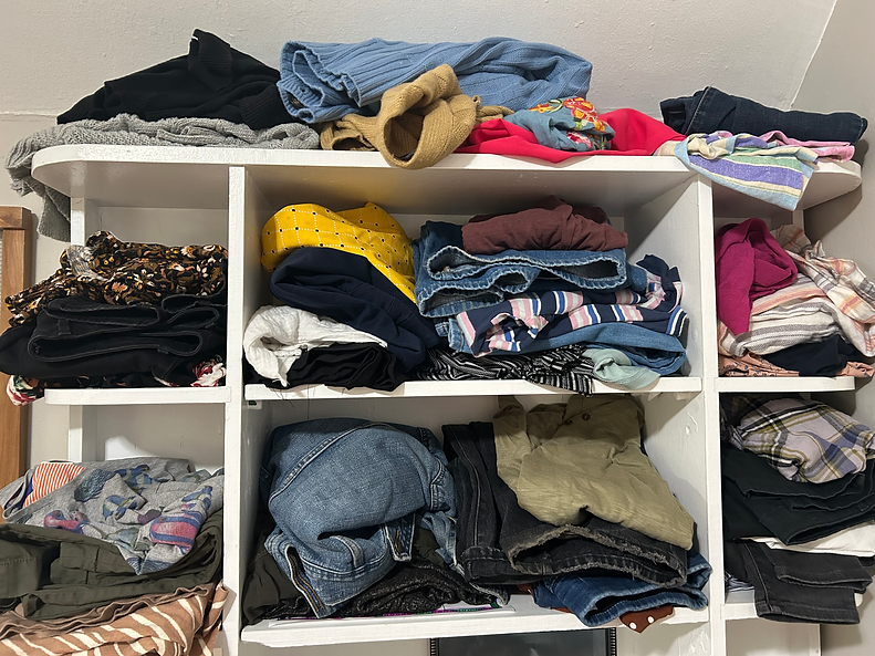 A mom puts her laundry away on shelves by sorting the clothes into outfits of the day