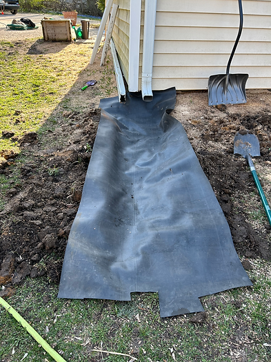 a large piece of plastic placed near the downspout to make a water feature. Two shovels are placed near the plastic.