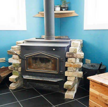A black wood-burning stove surrounded with spaving bricks and placed in the corner of a newly renovated Milwaukee Bungalow with a bright blue wall