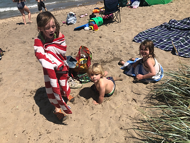 three kids warm up in the sand after swimming in Lake Michigan at Bender Beach