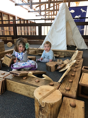 A toddler and baby play with wooden blocks and a teepee in the upper area of Havenwoods State Forest