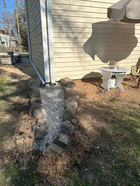 a completed water feature made with river rocks, river pebbles, large rocks and located at the back of the house near a mud kitchen