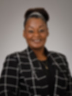 Professional headshot of a smiling woman with her hair in a bun, wearing a black and white plaid blazer.