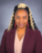 A woman with black and blonde braids wearing a maroon jacket and a blush colored blouse with matching earrings.