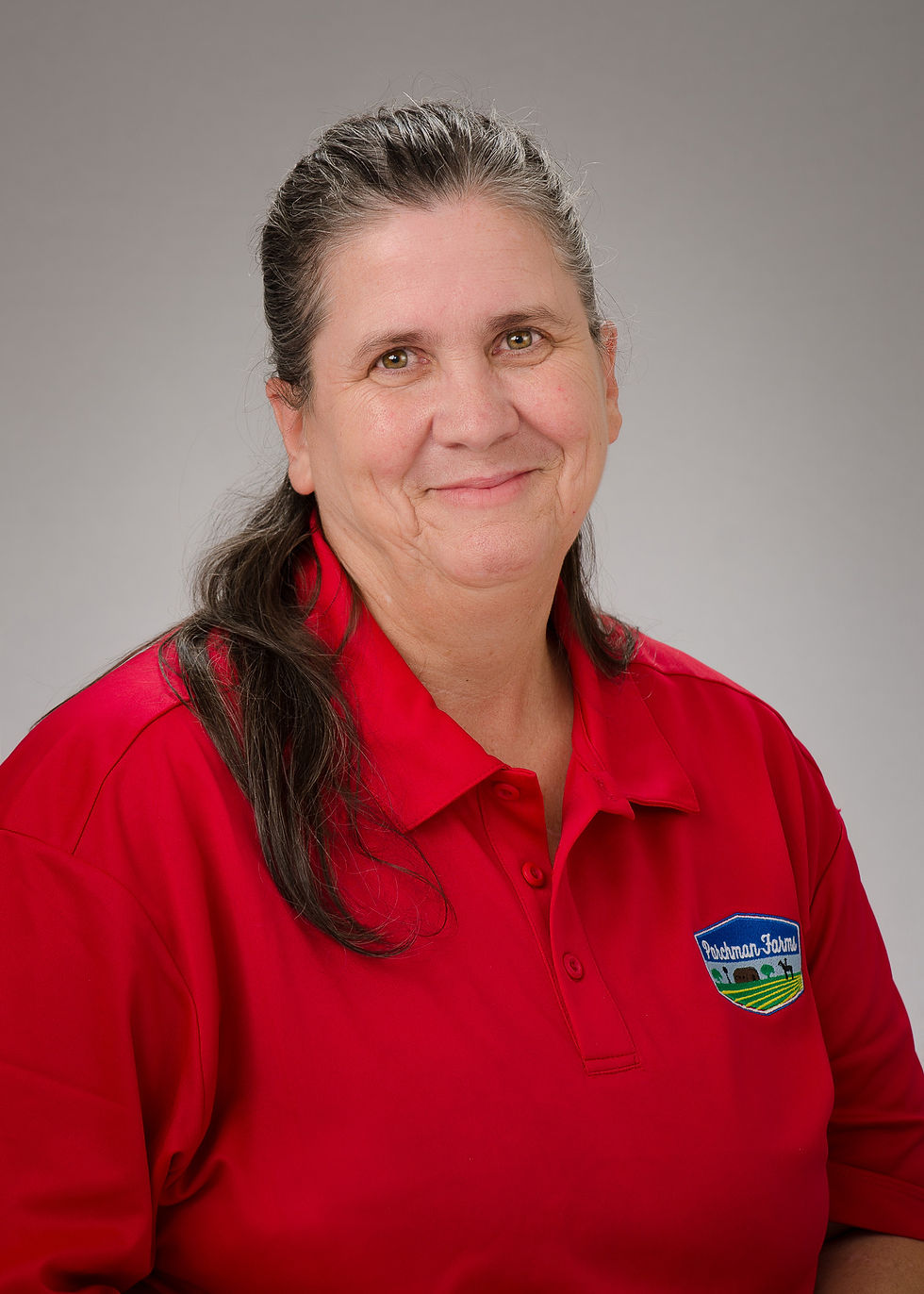 A woman with gay/brown hair wearing a red polo with Parchman Farms logo on it. 