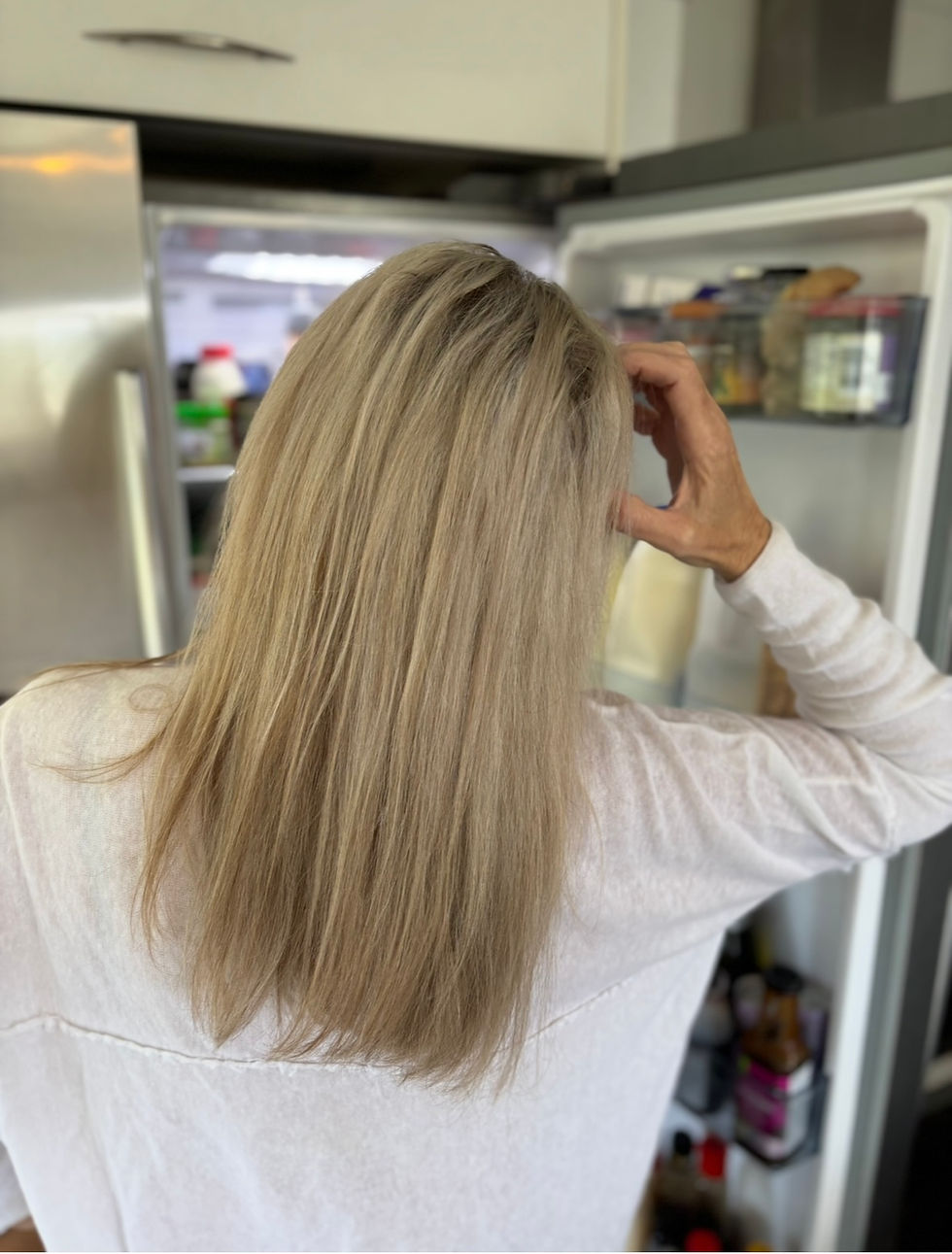 Woman looking worriedly into fridge, her hand on her head in exasperation, indicating she is berating herself .