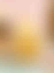 Cupcake with pineapple filling and frosting, topped with a pineapple decoration. Set on a plate with a fork, against a pastel backdrop.