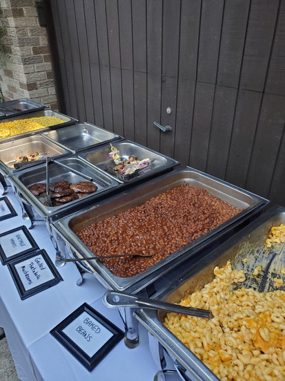 Buffet table with macaroni and cheese, buttered corn, baked beans, and pasta salad