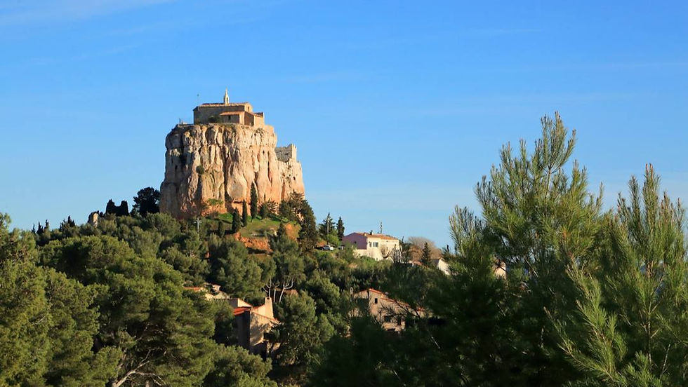 Rocher escarpé surmonté d’une chapelle, entouré de pins et de maisons, sous un ciel bleu dégagé.