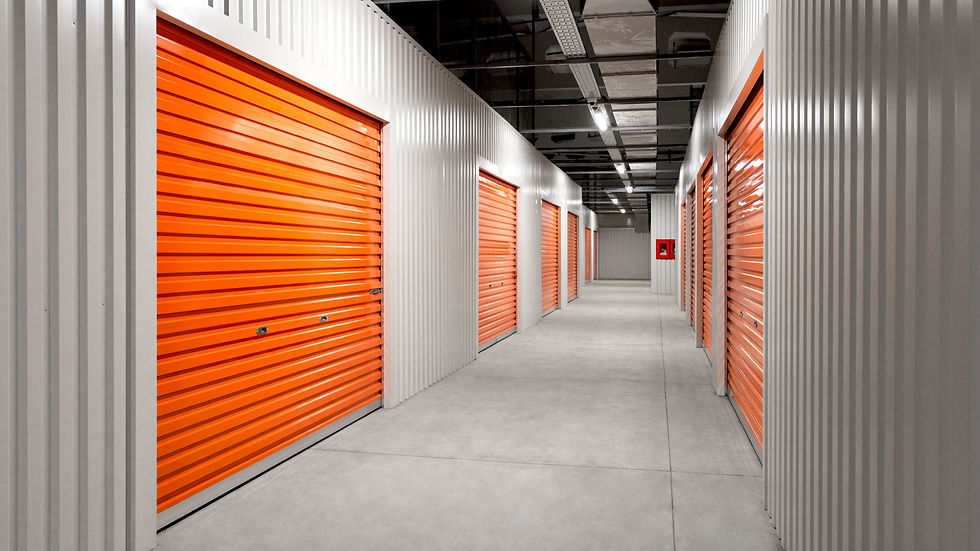 Couloir de box de stockage vides, portes roulantes orange et murs métalliques gris sous éclairage industriel.