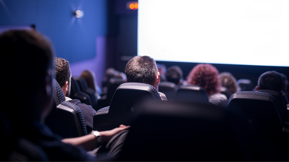 Public assis dans une salle de cinéma sombre, regardant un grand écran blanc lumineux.