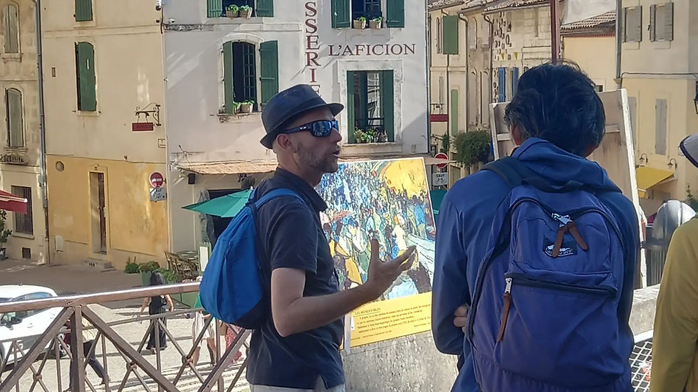 Deux hommes à dos bleus discutent devant des façades méditerranéennes, une affiche artistique et le texte L’AFICION.