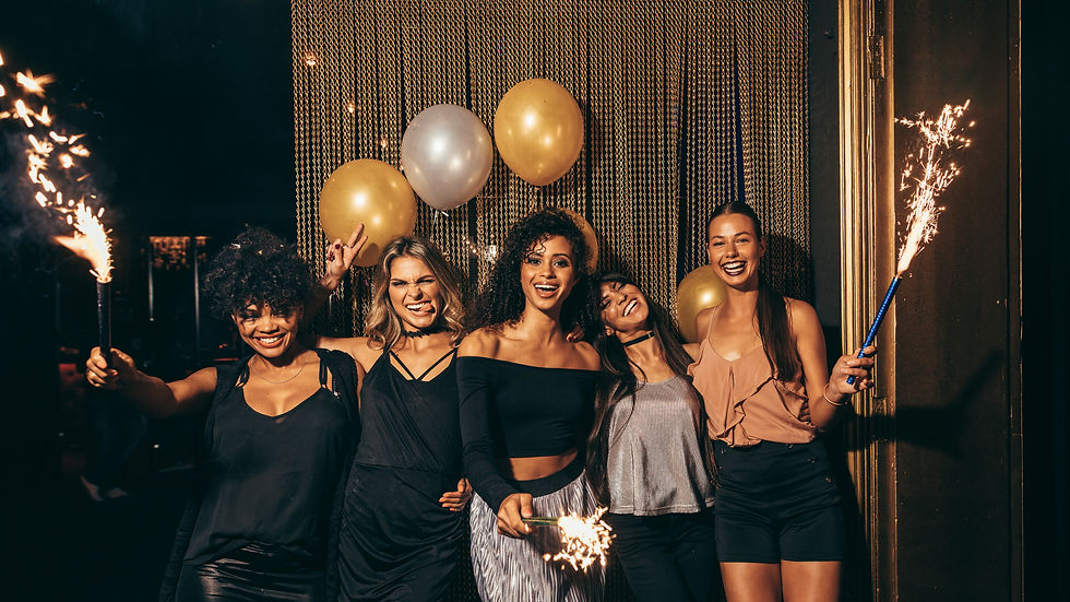Cinq femmes souriantes posent avec ballons dorés et feux de Bengale lors d’une fête chic et joyeuse.