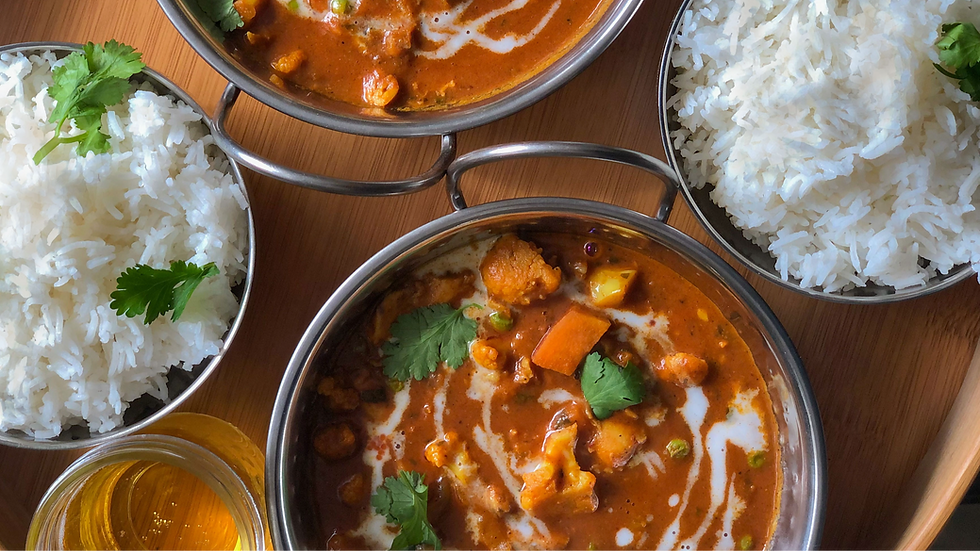 Curry orange dans trois bols avec riz blanc, coriandre et un verre de boisson, sur une table en bois.