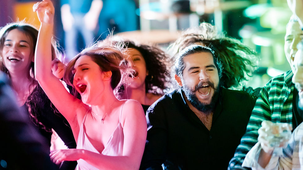 Groupe de jeunes danse et chante en concert, lumières rose et verte, visages enthousiastes dans une ambiance festive.