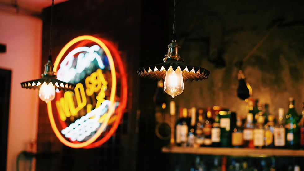 Bar tamisé avec ampoules suspendues et enseigne néon floue, bouteilles en arrière-plan, ambiance chaleureuse.