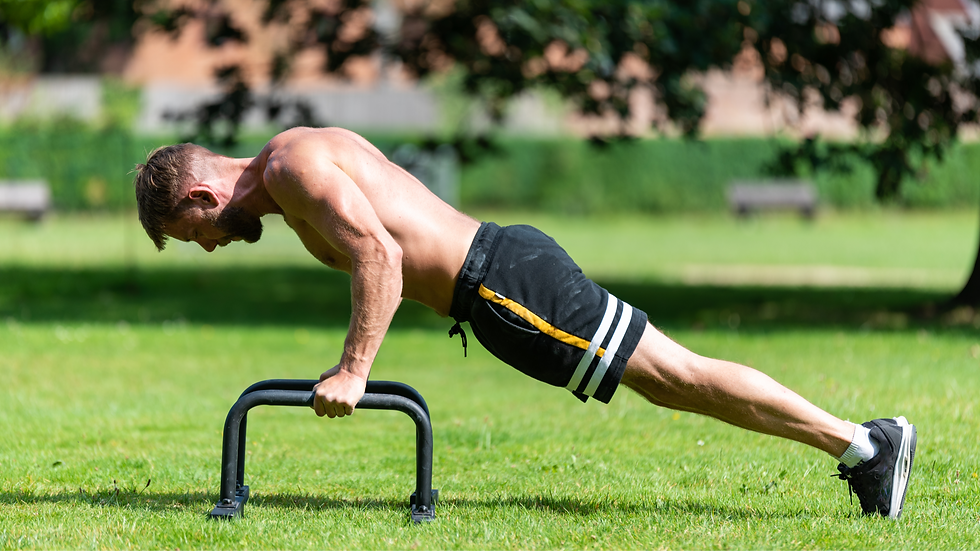 Homme torse nu faisant des pompes sur des barres parallèles dans un parc verdoyant, en plein effort sous le soleil.
