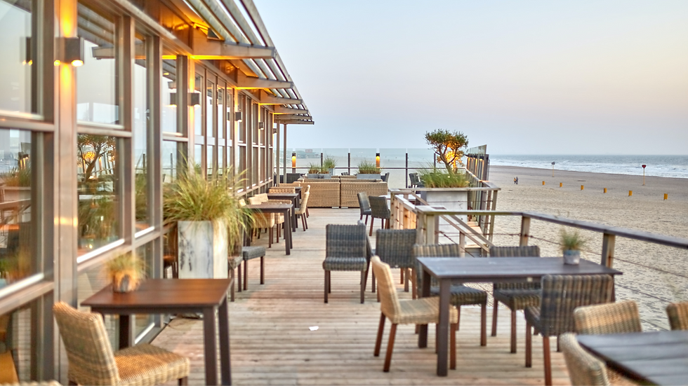 Terrasse de restaurant vide sur la plage, tables et chaises en bois, vue sur l’océan, lumières chaudes au coucher du soleil.