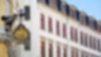 Enseigne dorée HOTEL sur façade d’immeuble ancien aux fenêtres rouges, sous ciel bleu.
