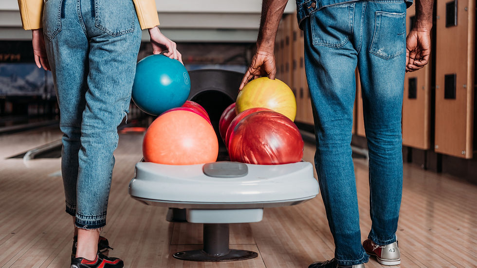 Deux personnes de dos, en jeans, dans une salle de bowling, choisissent des boules de couleurs vives sur la piste en bois.