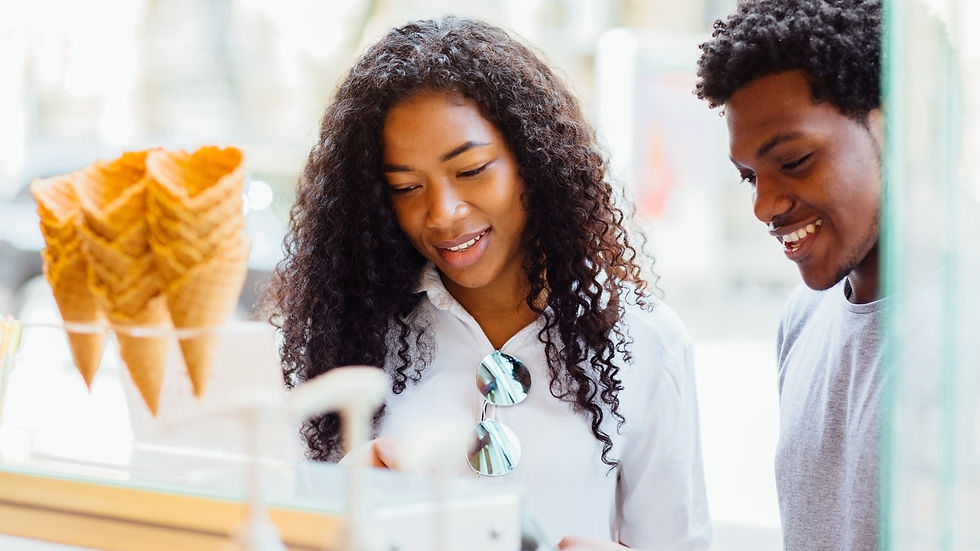 Deux jeunes adultes souriants choisissent des glaces en cornet dans une boutique lumineuse.