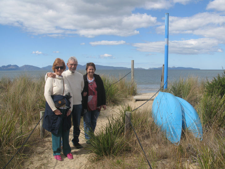Three people posing by a beach with blue paddles.