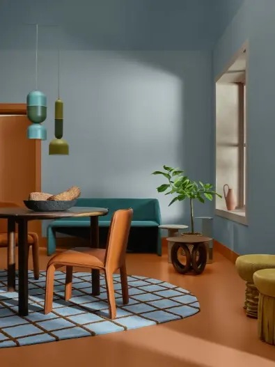 Uma sala de jantar com mesa, cadeira, tapete, um sofá ao fundo e uma janela na lateral direita