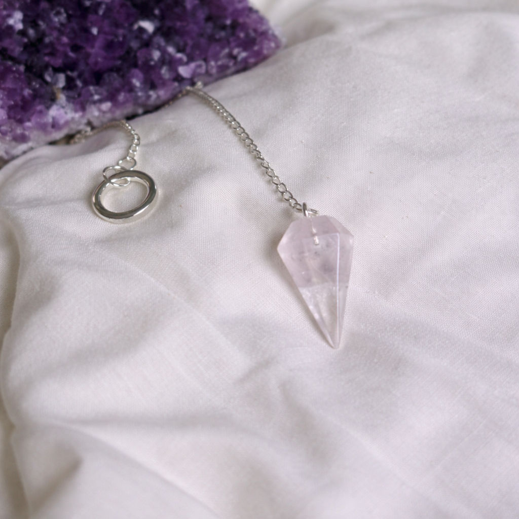 Pink crystal pendulum with amethyst on white fabric