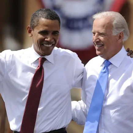 Two men in white shirts and ties (Barack Obama, left, and Joe Biden) wave and smile outdoors, appearing joyful. A patriotic banner is blurred in the background.