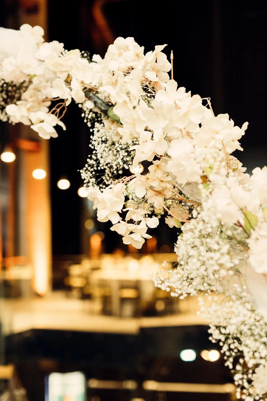 Arche décorée de fleurs blanches pour un mariage, avec un fond flou de tables dressées.