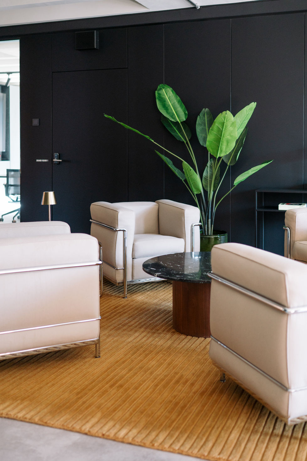 Contemporary office lounge in Frankfurt with neutral armchairs, black marble coffee table, and dark paneled walls.