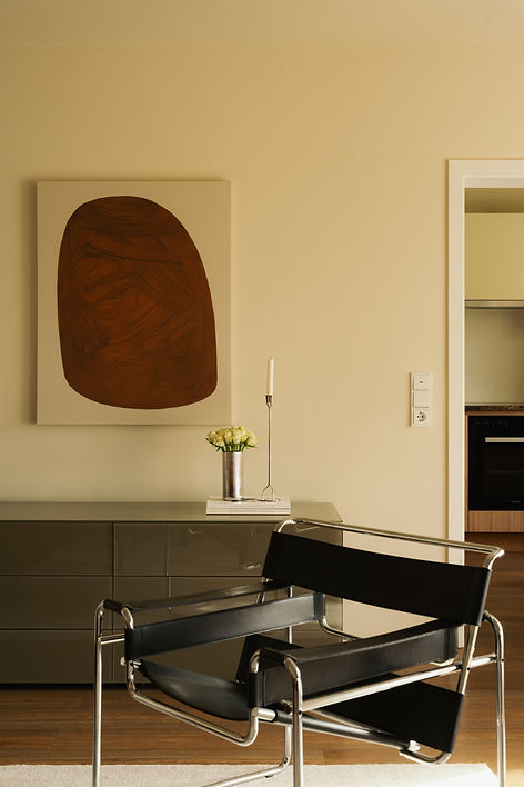Svart läderfåtölj med kromad stålram framför sideboard med marmorlampa, silverljusstake och storskaligt konstverk i rostbrunt