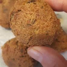 Hand holding crispy vegan falafel and more falafel in the background