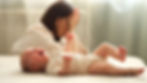 Tired infant girl cries on double bed against depressed mother sitting on floor. Baby daug