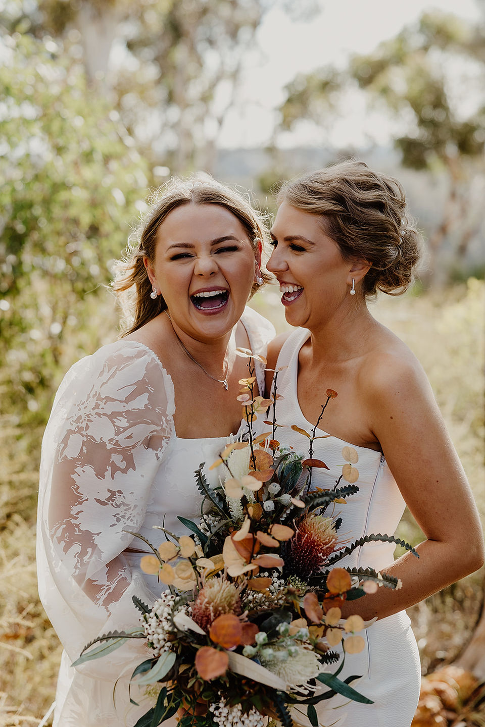 Two brides wear white dresses and hold bouquets in the Australian bush at Anderson Point in the Perth Hills