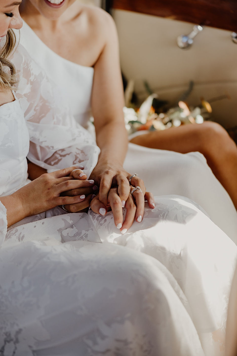 Two brides sit in a white classic Rolls Royce and hold hands cuddling in the car, just outside their Anderson Point ceremony in the Perth Hills.