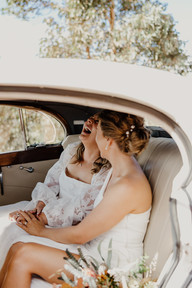 Two brides sit in a classic white Rolls Royce as they cuddle and smile with each other, holding hands and laughing together. Their wedding ceremony is at Anderson Point in the Perth HIlls.