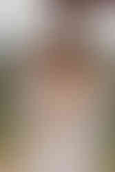 A bride laughs during the wedding ceremony, holding her brides hand and the celebrant standing nearby. They stand under a wooden arbor adorned with flowers.