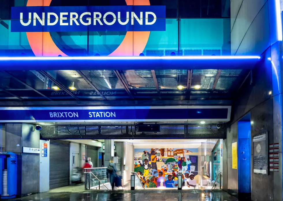 Brixton Station entrance at night with vibrant mural; people walking. Signs read "UNDERGROUND" and "BRIXTON STATION." Blue lighting.