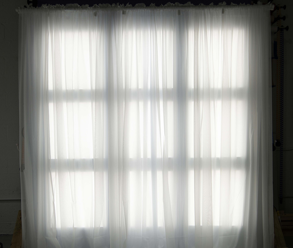 White sheer curtains covering a large window in a studio.