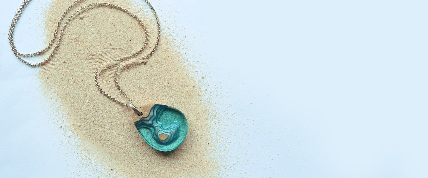 Turquoise pendant and silver chain on sand