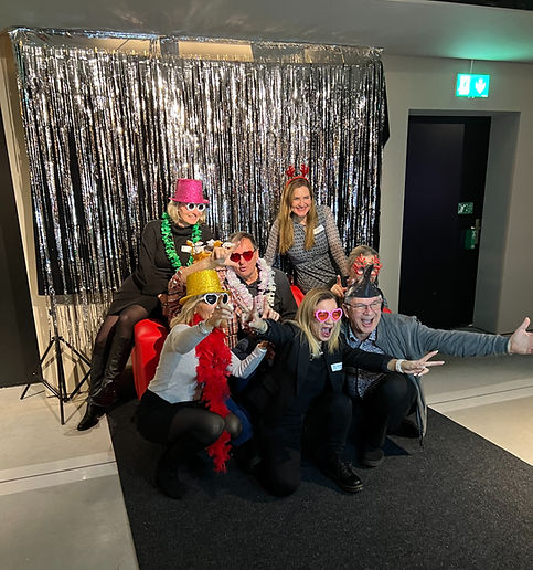 Fotobox Weihnachtsfeier in Lenzburg – Mitarbeitende posieren vor der SnapBox Fotobox Large mit elegantem glitzer Hintergrund aus Lametta, Lichterketten und Geschenken. Spassige Erinnerungsfotos für Weihnachtsfeiern und Teamevents im Kanton Aargau, Zürich, Basel und Solothurnu, .