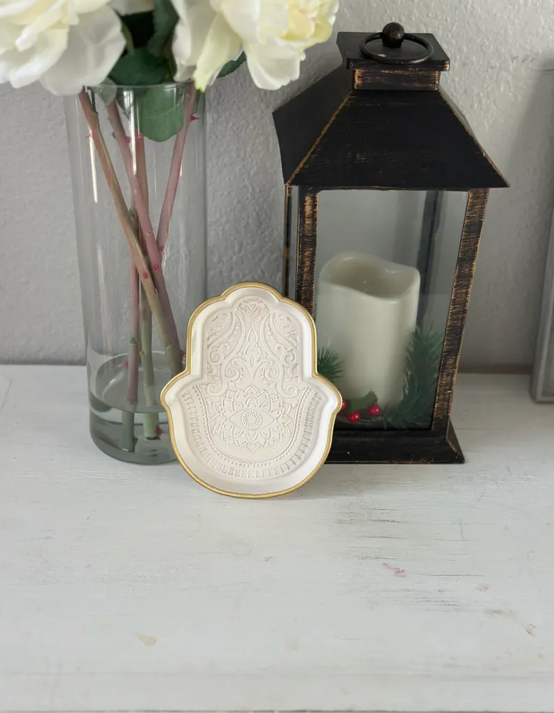 White hand-shaped dish with floral details next to a candle lantern.