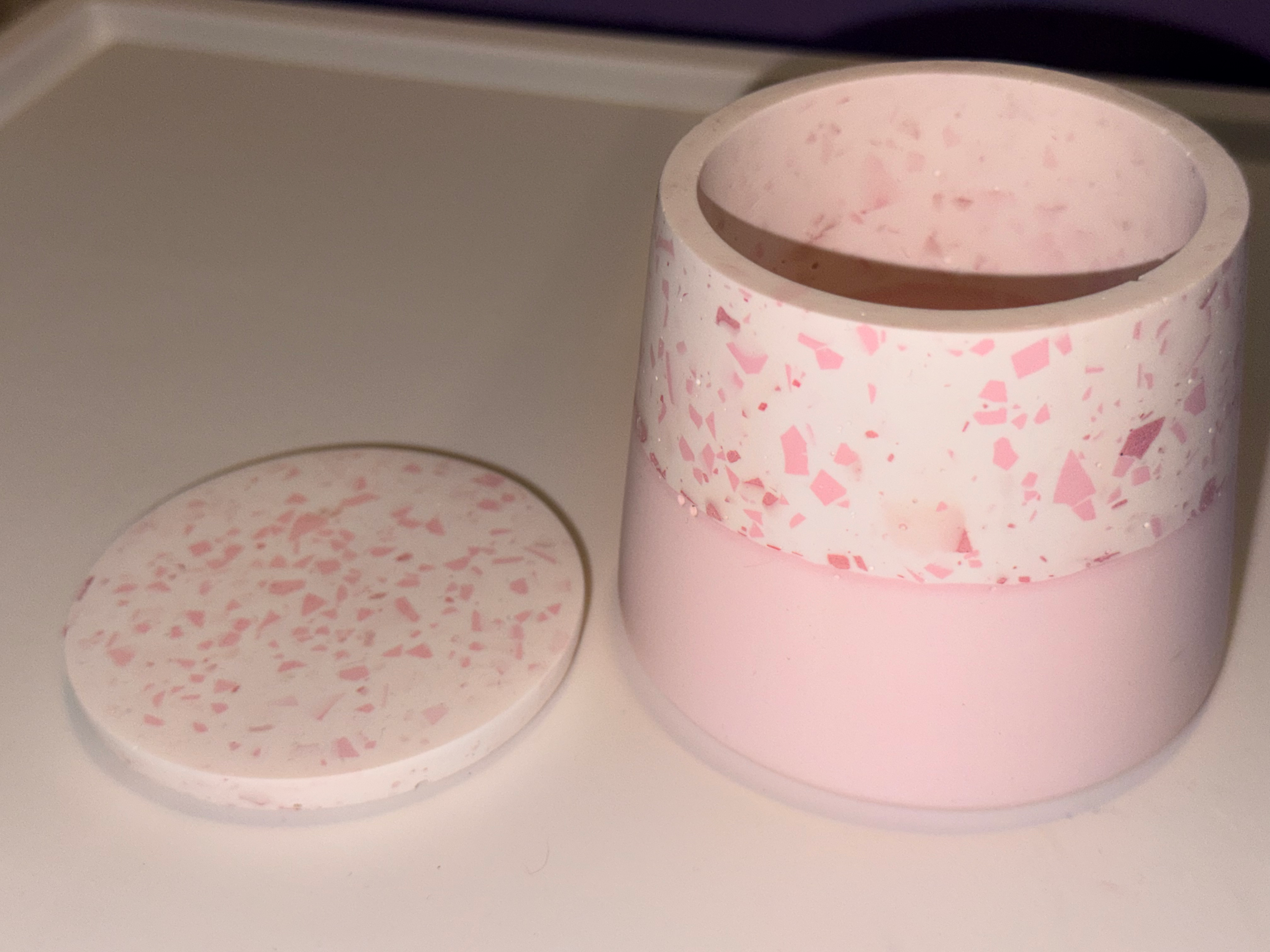 Pink terrazzo style container and lid on white surface, close-up shot.