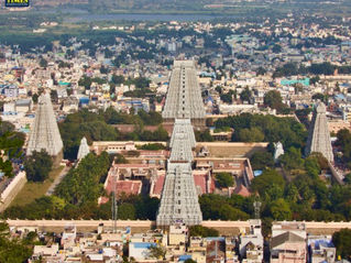 Aerial view of a cityscape with large temple towers surrounded by trees and buildings. The sky is clear. "Tour Times" text is visible. Temples in Tamil Nadu