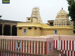 Hindu temple complex with cream towers behind a red-and-white striped wall, Tour Times logo in the top left. Azhagiya Manavala Perumal