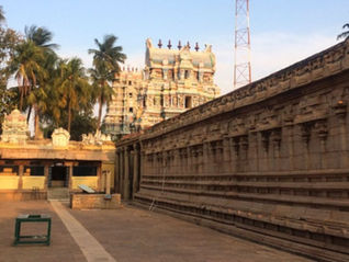 Sunlit South Indian temple courtyard with ornate gopuram, palm trees, and long stone walls; Tour Times logo at top right. Thirumohoor Kalamegaperumal Temple